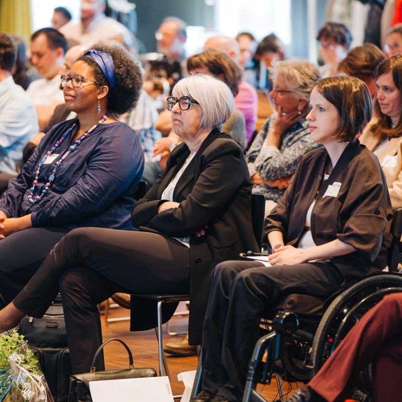 Teilnehmende sitzen dicht nebeneinander im Publikum der Delegiertenversammlung 2026 von Agile und hören aufmerksam einer Präsentation zu. Im Vordergrund sind mehrere Personen in einer Sitzreihe zu sehen, dahinter weitere Teilnehmende im gut gefüllten Veranstaltungsraum.